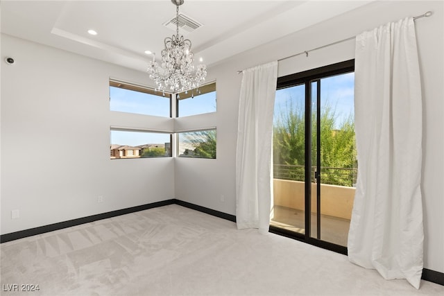 spare room with a raised ceiling, light colored carpet, an inviting chandelier, and plenty of natural light