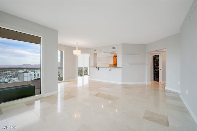 unfurnished living room with light tile patterned flooring, stacked washer / dryer, a healthy amount of sunlight, and a notable chandelier