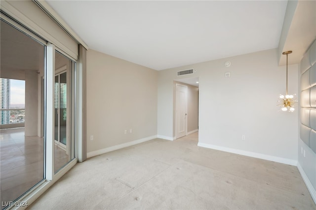 empty room with light colored carpet and an inviting chandelier