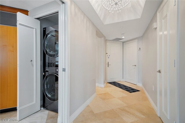 clothes washing area featuring stacked washer / dryer, light tile patterned floors, and a notable chandelier