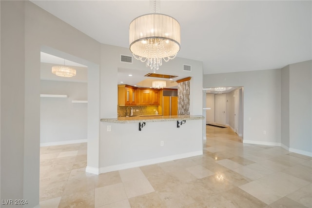 kitchen featuring an inviting chandelier, decorative backsplash, light stone counters, a kitchen bar, and kitchen peninsula