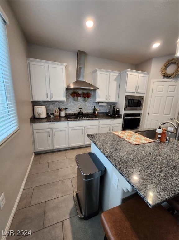 kitchen with appliances with stainless steel finishes, wall chimney range hood, white cabinets, and dark stone counters