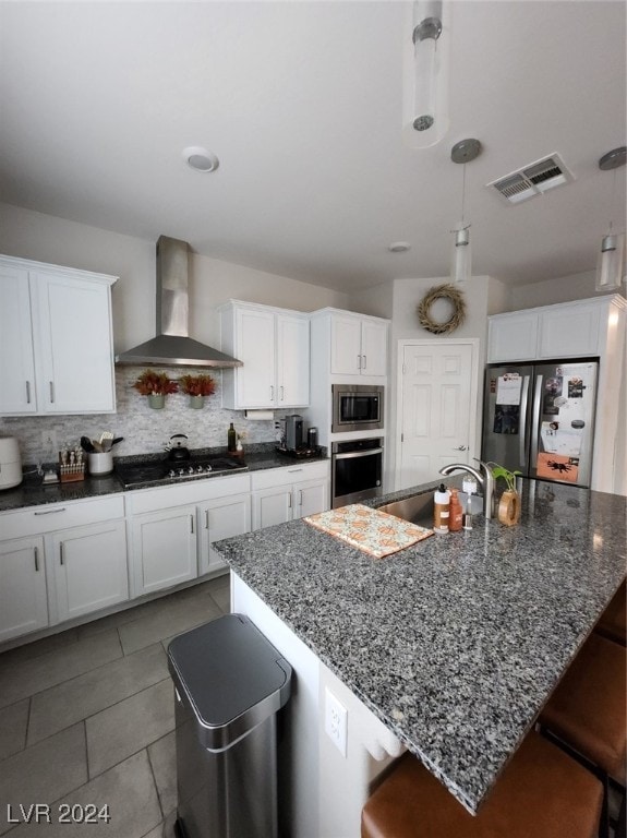 kitchen with wall chimney range hood, stainless steel appliances, backsplash, a large island, and white cabinets