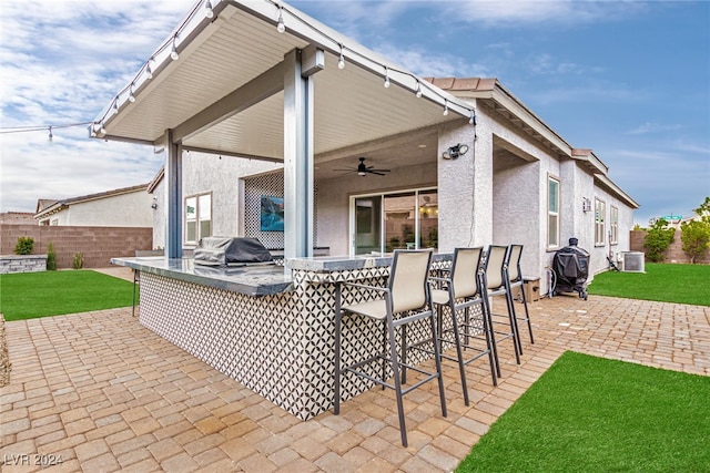 view of patio with grilling area, ceiling fan, a bar, and an outdoor kitchen