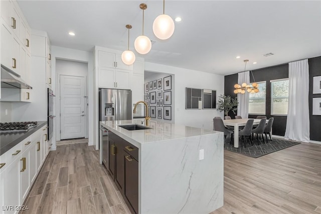 kitchen with sink, pendant lighting, a center island with sink, white cabinets, and a chandelier