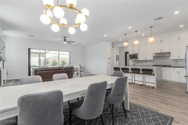 dining space featuring wood-type flooring, ceiling fan with notable chandelier, and sink