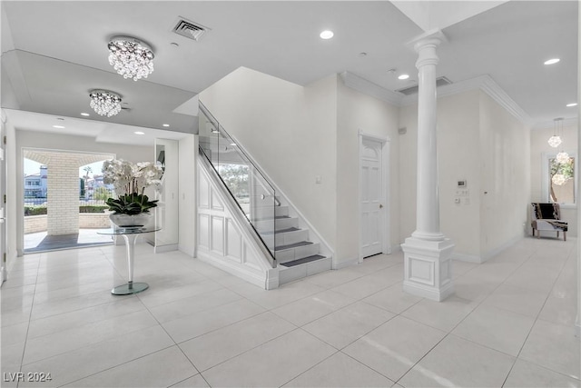 staircase featuring tile patterned floors, ornate columns, ornamental molding, and a notable chandelier