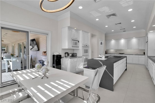 kitchen with white microwave, crown molding, white cabinets, an island with sink, and light tile patterned flooring