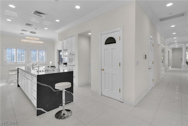 kitchen with crown molding, white cabinetry, a kitchen island with sink, and light tile patterned floors