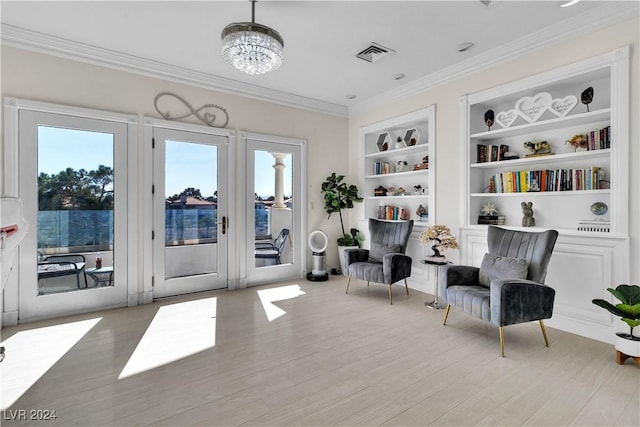 sitting room featuring a chandelier, built in shelves, light hardwood / wood-style floors, and crown molding