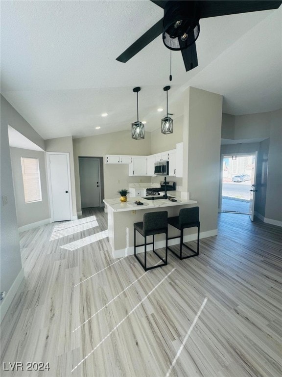 kitchen featuring light wood-type flooring, kitchen peninsula, stainless steel appliances, lofted ceiling, and white cabinets