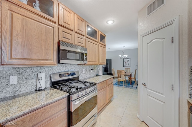 kitchen featuring stainless steel appliances, a notable chandelier, light tile patterned floors, light stone counters, and tasteful backsplash