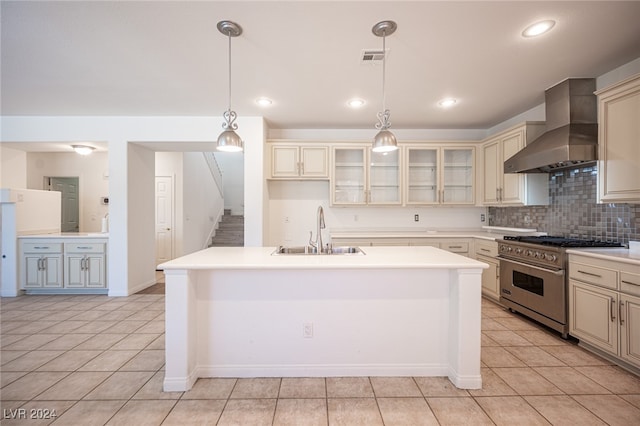 kitchen featuring cream cabinets, wall chimney range hood, sink, high end stove, and decorative light fixtures