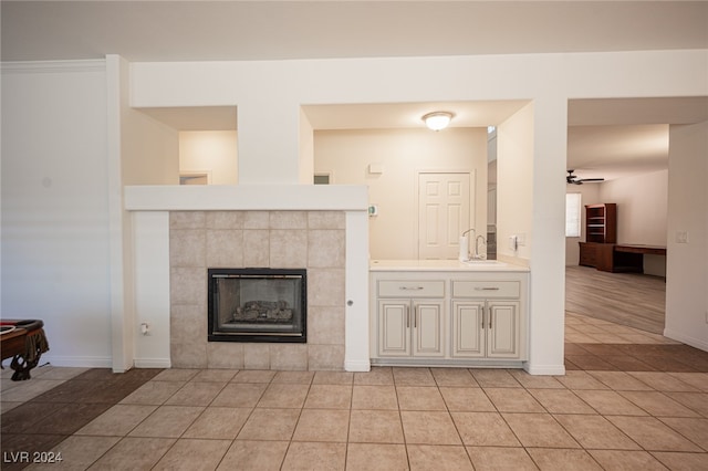 unfurnished living room featuring ceiling fan, light tile patterned floors, sink, and a tiled fireplace