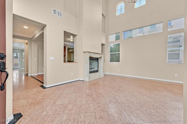 unfurnished living room featuring a high end fireplace, a healthy amount of sunlight, and a high ceiling