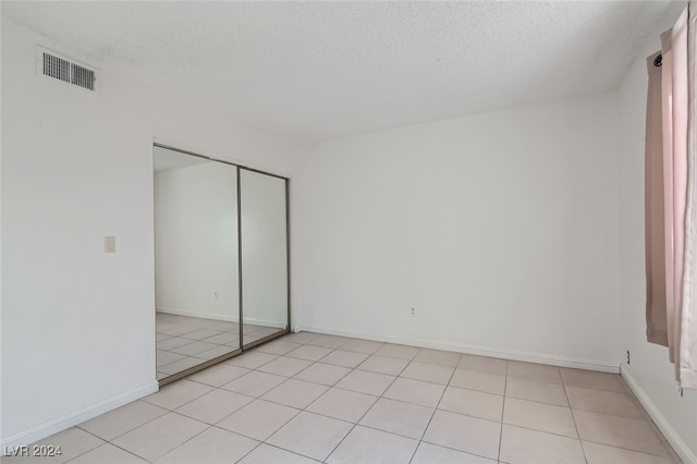 unfurnished bedroom featuring a closet, a textured ceiling, and light tile patterned floors