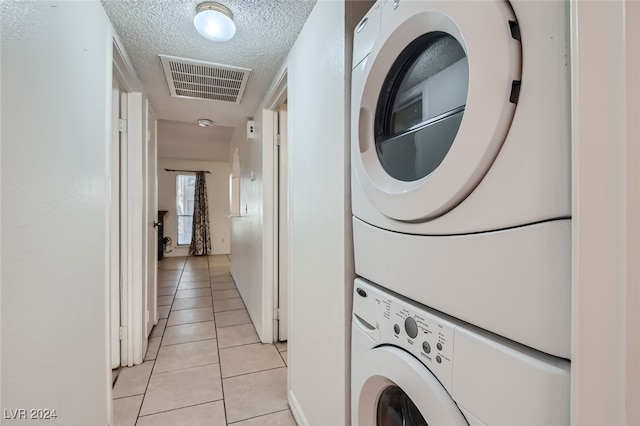 laundry room featuring a textured ceiling, light tile patterned floors, and stacked washer and clothes dryer