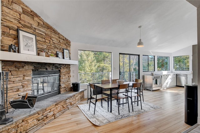 dining space featuring light hardwood / wood-style floors, lofted ceiling, and a stone fireplace