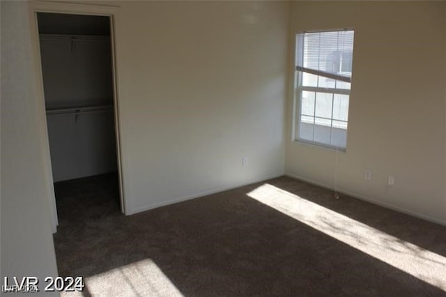 unfurnished bedroom with dark carpet, a closet, and a spacious closet