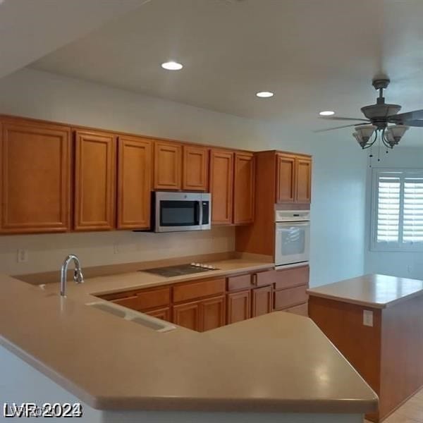 kitchen featuring sink, white oven, kitchen peninsula, ceiling fan, and stovetop