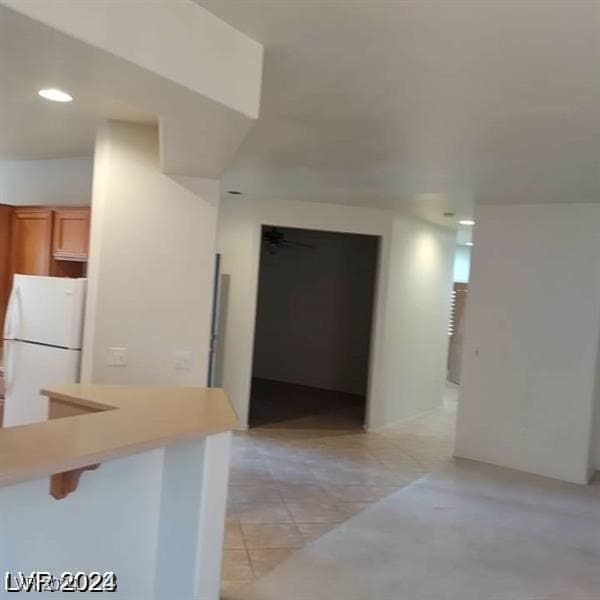 kitchen featuring a kitchen breakfast bar, kitchen peninsula, light tile patterned floors, and white refrigerator