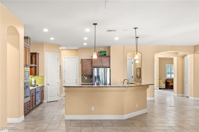 kitchen with decorative backsplash, appliances with stainless steel finishes, decorative light fixtures, and a kitchen island with sink