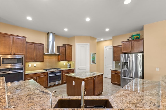 kitchen with sink, appliances with stainless steel finishes, light stone countertops, a kitchen island, and wall chimney range hood