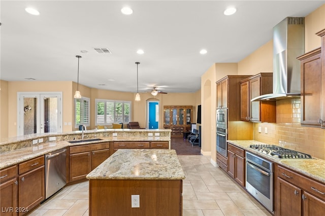 kitchen with stainless steel appliances, a center island, wall chimney exhaust hood, sink, and decorative light fixtures