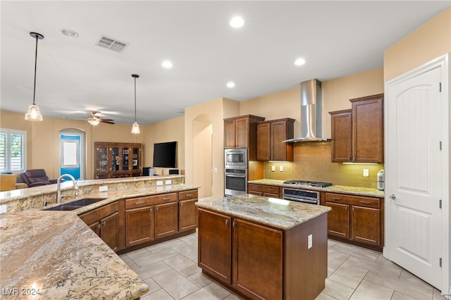 kitchen featuring wall chimney exhaust hood, sink, a large island, ceiling fan, and pendant lighting