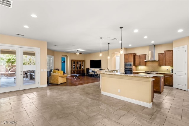 kitchen with stainless steel appliances, wall chimney exhaust hood, hanging light fixtures, a large island, and french doors