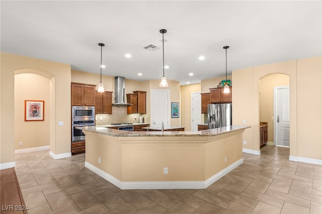 kitchen with stainless steel appliances, a large island with sink, tasteful backsplash, wall chimney exhaust hood, and decorative light fixtures