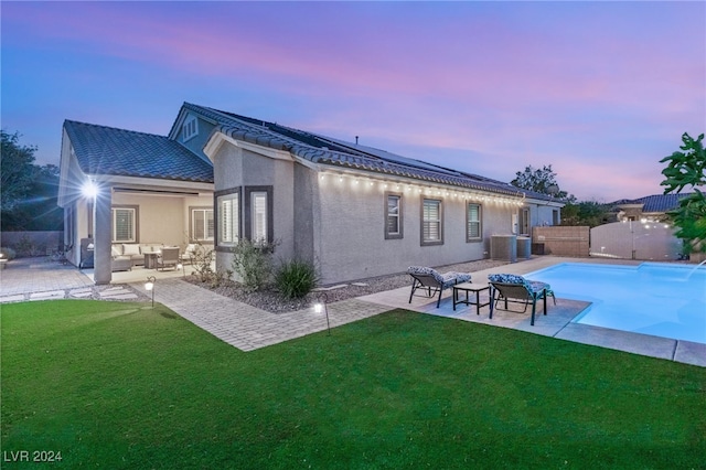 back house at dusk with an outdoor hangout area, a lawn, a fenced in pool, and a patio area