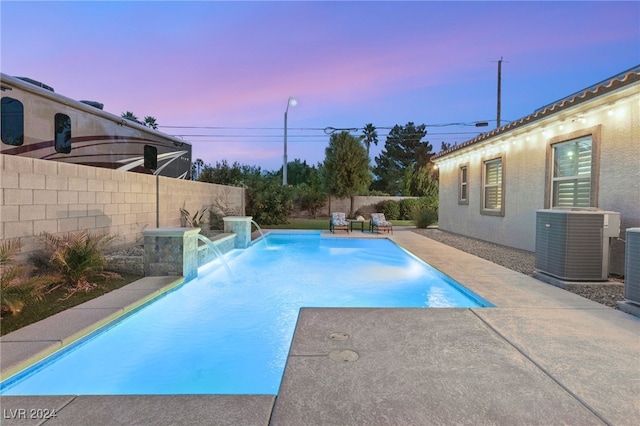 pool at dusk featuring central air condition unit and pool water feature