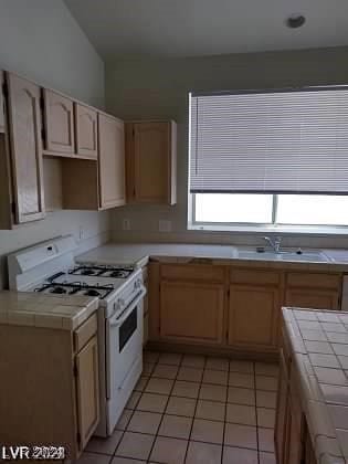 kitchen with tile countertops, light tile patterned floors, light brown cabinets, and gas range gas stove