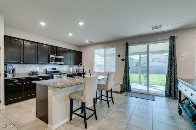 4323 Creekside Cavern Ave, North Las Vegas, NV 89084 - kitchen featuring stainless steel appliances, a sink, a kitchen bar, light stone counters, and tasteful backsplash