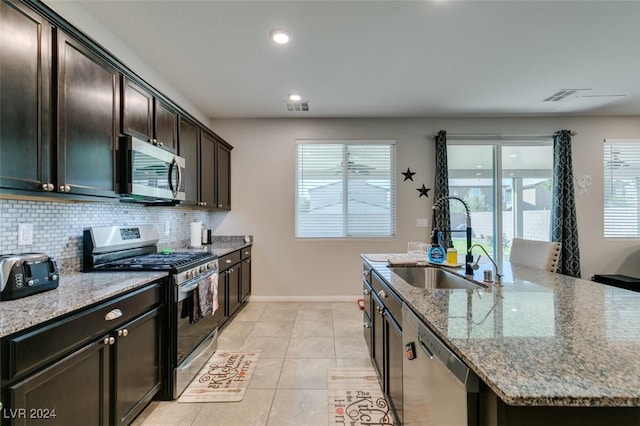 4323 Creekside Cavern Ave, North Las Vegas, NV 89084 - kitchen with stainless steel appliances, a sink, baseboards, stone countertops, and an island with sink