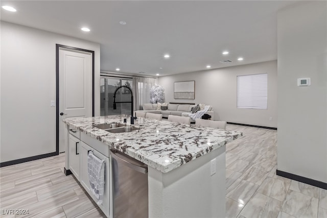 kitchen with light stone countertops, sink, an island with sink, dishwasher, and white cabinetry