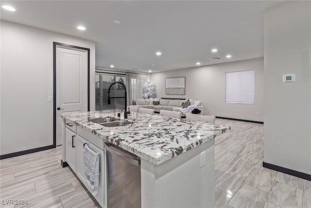 kitchen featuring light stone countertops, a sink, recessed lighting, baseboards, and a center island with sink