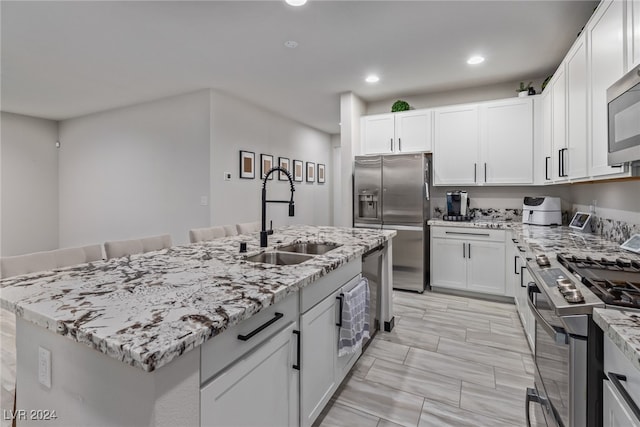 kitchen featuring a kitchen island with sink, stainless steel appliances, sink, light stone countertops, and white cabinets