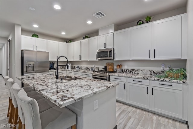 kitchen with a kitchen island with sink, sink, white cabinets, a kitchen bar, and appliances with stainless steel finishes