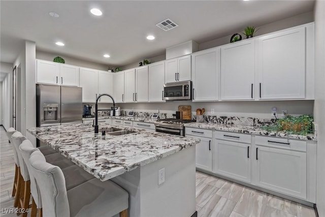 kitchen featuring visible vents, a breakfast bar, light stone countertops, a sink, and stainless steel appliances