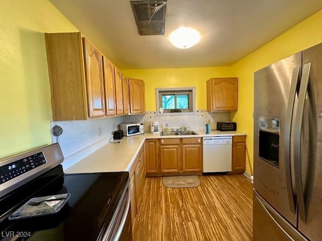 kitchen featuring appliances with stainless steel finishes, light wood-type flooring, tasteful backsplash, and sink