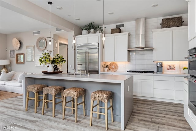 kitchen with wall chimney range hood, a breakfast bar area, appliances with stainless steel finishes, white cabinetry, and light hardwood / wood-style flooring