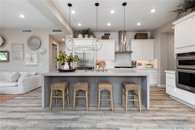 kitchen with wall chimney exhaust hood, appliances with stainless steel finishes, a breakfast bar, and a kitchen island with sink