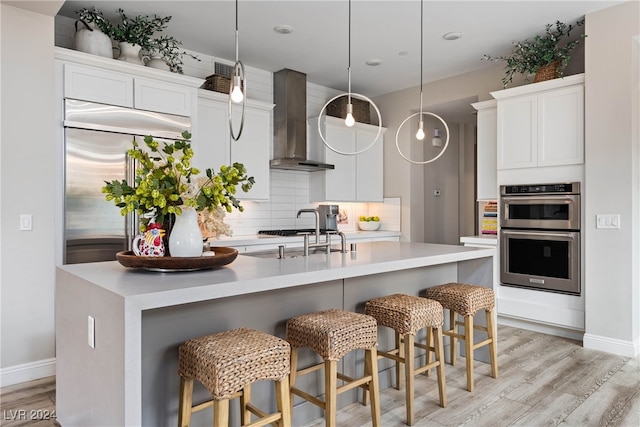 kitchen with wall chimney exhaust hood, white cabinetry, hanging light fixtures, and stainless steel appliances