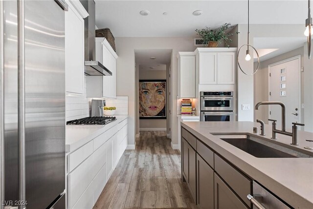 kitchen featuring white cabinets, hanging light fixtures, light hardwood / wood-style flooring, sink, and stainless steel appliances