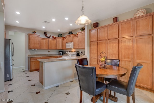 kitchen featuring light stone counters, stainless steel refrigerator, light tile patterned flooring, sink, and decorative light fixtures