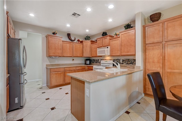 kitchen with kitchen peninsula, light stone counters, light tile patterned floors, sink, and white appliances