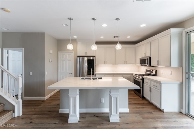 kitchen featuring stainless steel appliances, decorative light fixtures, light hardwood / wood-style floors, white cabinets, and a kitchen island with sink