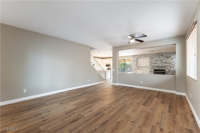 unfurnished living room featuring ceiling fan, wood-type flooring, plenty of natural light, and a stone fireplace